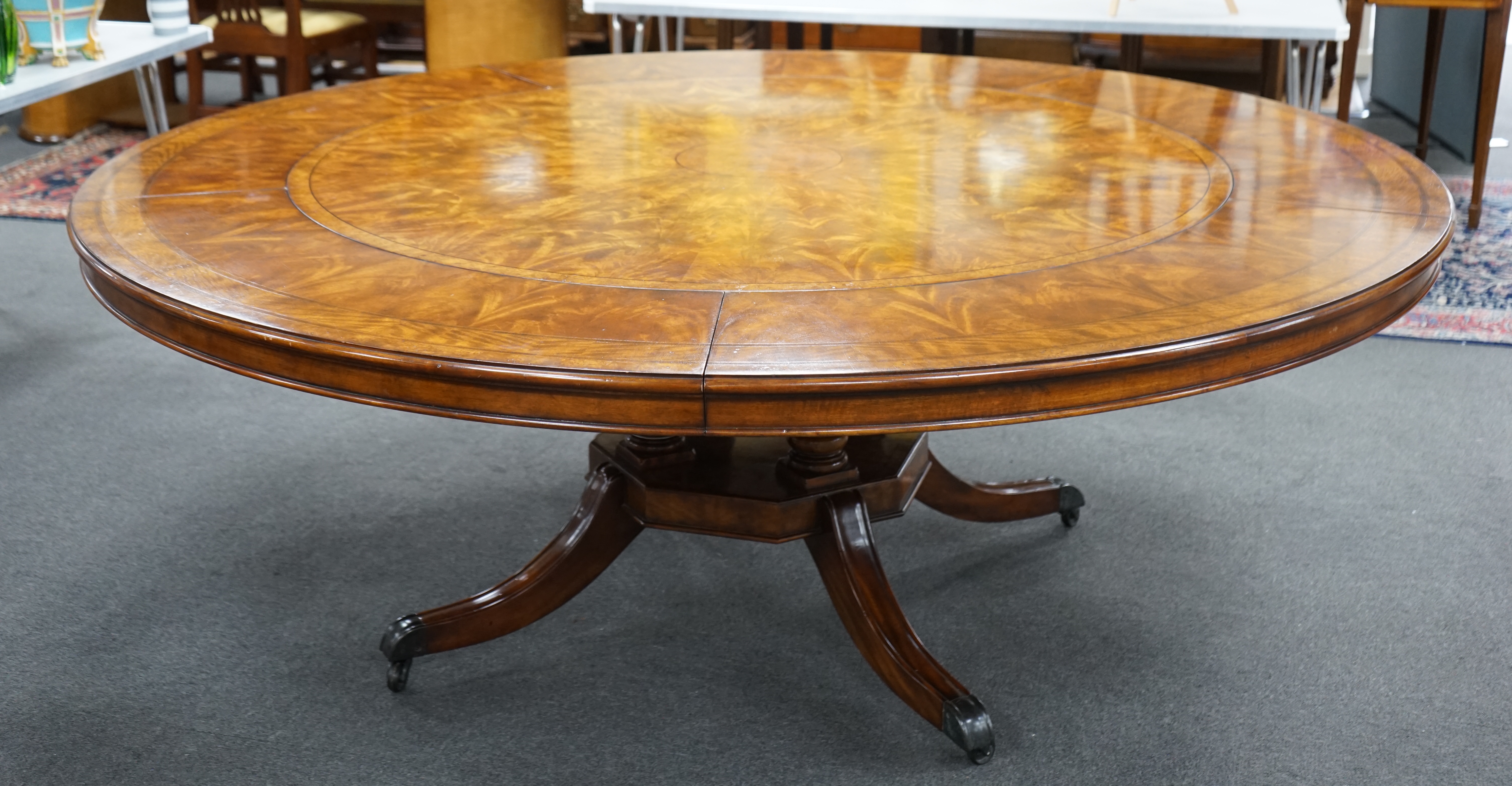 A reproduction George III style circular mahogany extending dining table with detachable segmental outer ring and eight Empire style cherry dining chairs with tan leather seats, table 142cm diameter, 202cm diameter exten